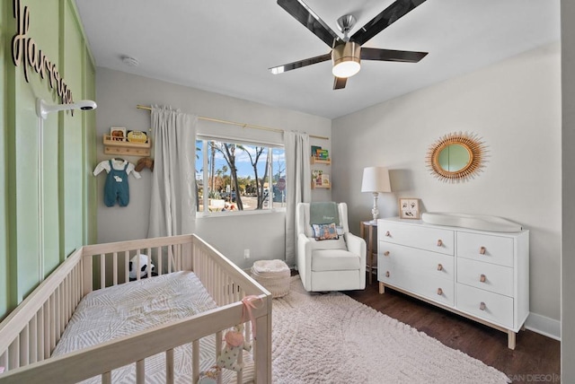 bedroom with dark wood-type flooring, ceiling fan, and a crib