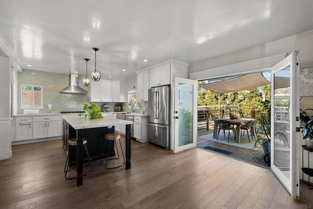 kitchen featuring high end fridge, hanging light fixtures, white cabinetry, and wall chimney exhaust hood