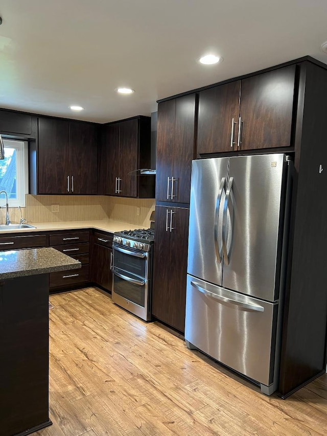 kitchen with sink, stainless steel appliances, dark brown cabinets, light wood-type flooring, and wall chimney exhaust hood