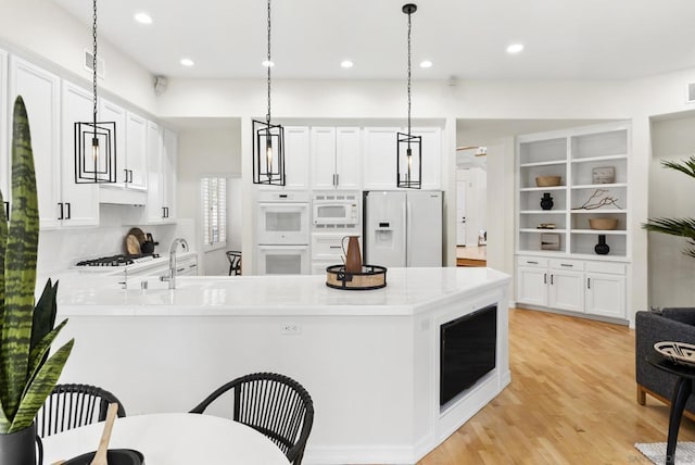 kitchen with pendant lighting, white appliances, kitchen peninsula, and white cabinets