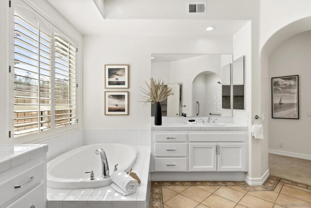 bathroom featuring tile patterned flooring, vanity, and tiled bath