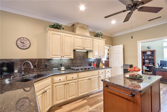 kitchen with stainless steel gas stovetop, tasteful backsplash, sink, dark stone counters, and light hardwood / wood-style floors