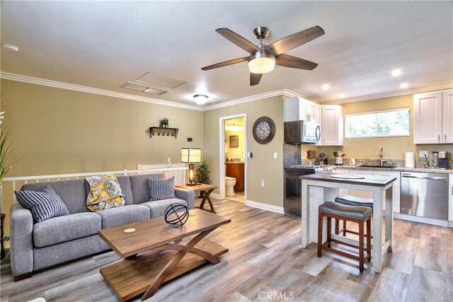 living room with crown molding, sink, and light wood-type flooring