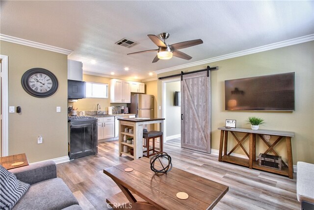 living room with sink, ceiling fan, crown molding, a barn door, and light hardwood / wood-style flooring