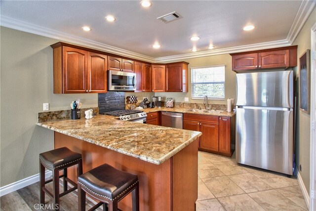 kitchen with appliances with stainless steel finishes, sink, light stone counters, and kitchen peninsula