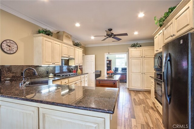 kitchen featuring sink, crown molding, dark stone countertops, light wood-type flooring, and black appliances