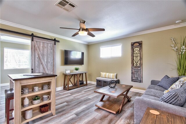 living room featuring crown molding, a barn door, ceiling fan, and light wood-type flooring