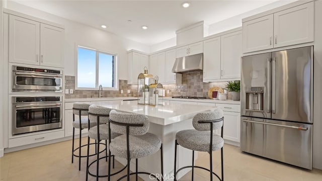 kitchen featuring a breakfast bar, tasteful backsplash, white cabinetry, a center island, and stainless steel appliances