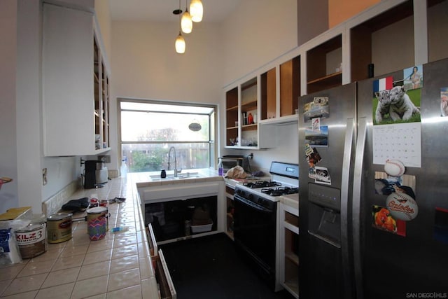 kitchen with sink, white cabinetry, light tile patterned floors, stainless steel fridge, and range with gas stovetop