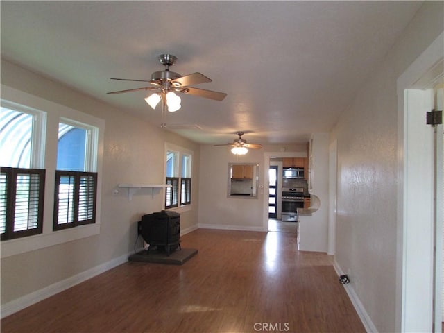 unfurnished living room with ceiling fan, hardwood / wood-style floors, and a wood stove