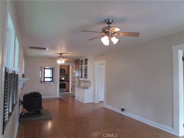 unfurnished living room featuring hardwood / wood-style floors, ceiling fan, and a wood stove