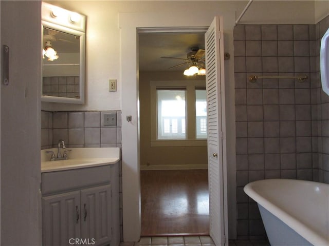 bathroom featuring vanity, tile walls, ceiling fan, and a tub to relax in