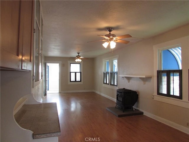 unfurnished living room featuring hardwood / wood-style flooring, ceiling fan, and a wood stove