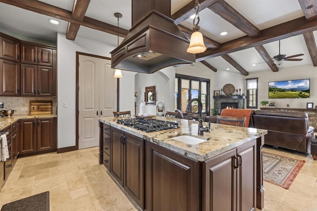 kitchen featuring stainless steel gas stovetop, decorative light fixtures, a kitchen island with sink, and dark brown cabinets