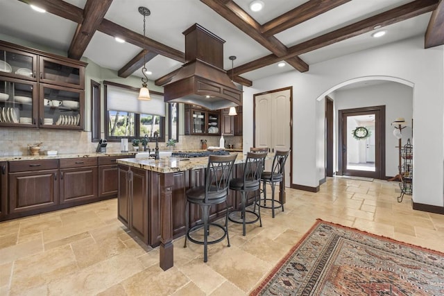 kitchen featuring dark brown cabinetry, tasteful backsplash, hanging light fixtures, a kitchen island, and light stone countertops