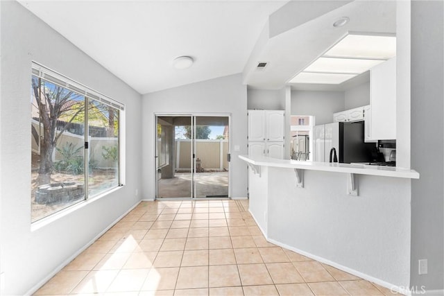 kitchen featuring vaulted ceiling, white cabinets, a kitchen breakfast bar, kitchen peninsula, and black fridge