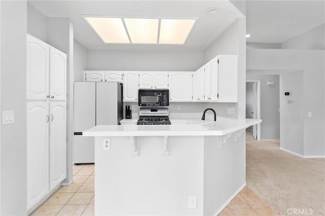 kitchen featuring stainless steel gas stove, white cabinetry, a kitchen breakfast bar, fridge, and kitchen peninsula