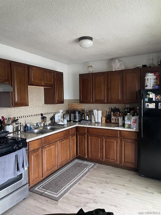 kitchen featuring sink, gas stove, tasteful backsplash, light hardwood / wood-style flooring, and black refrigerator