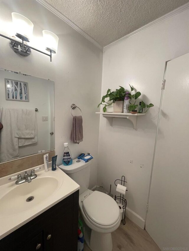 bathroom with hardwood / wood-style floors, vanity, toilet, crown molding, and a textured ceiling