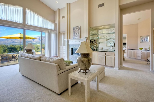 living room with light carpet, a towering ceiling, and a tile fireplace