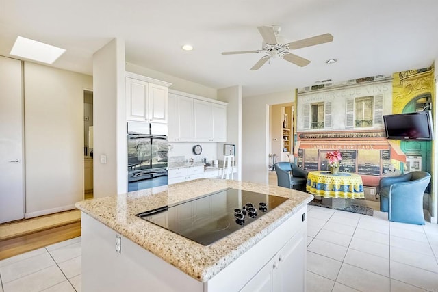 kitchen featuring light tile patterned flooring, multiple ovens, a skylight, white cabinets, and black electric stovetop