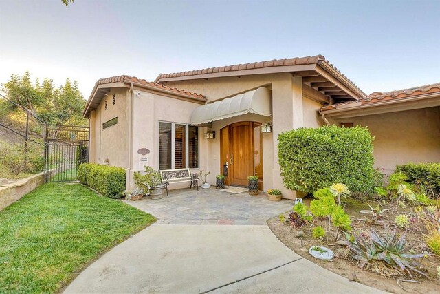 15615 Pauma Valley Dr, Pauma Valley, CA 92061 - view of exterior entry featuring a gate, a tile roof, a lawn, and stucco siding