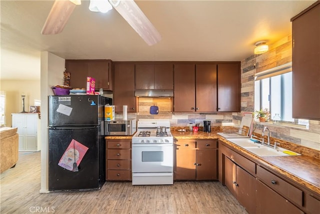 kitchen featuring sink, backsplash, black fridge, white gas stove, and light wood-type flooring