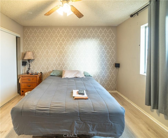 bedroom with multiple windows, ceiling fan, light hardwood / wood-style floors, a textured ceiling, and a closet