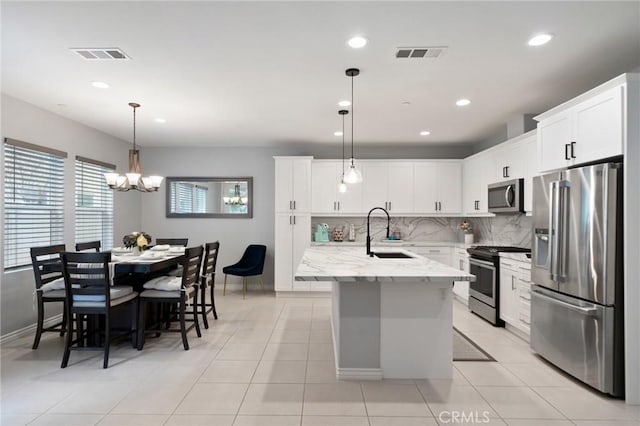 kitchen featuring pendant lighting, sink, stainless steel appliances, light stone countertops, and a center island with sink