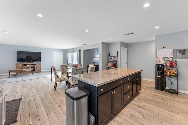 kitchen with light stone countertops, a kitchen island, dark brown cabinets, and light hardwood / wood-style floors