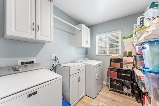 clothes washing area with cabinets, washer and clothes dryer, and light hardwood / wood-style flooring