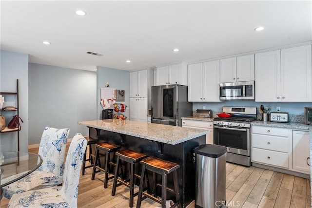 kitchen with appliances with stainless steel finishes, light hardwood / wood-style flooring, a kitchen island, and white cabinets