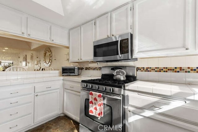 kitchen featuring stainless steel appliances, white cabinetry, tasteful backsplash, and tile countertops