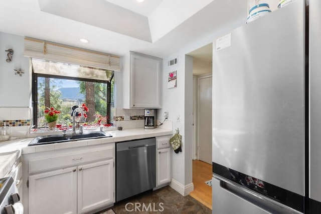 kitchen featuring sink, white cabinetry, tasteful backsplash, a raised ceiling, and stainless steel appliances