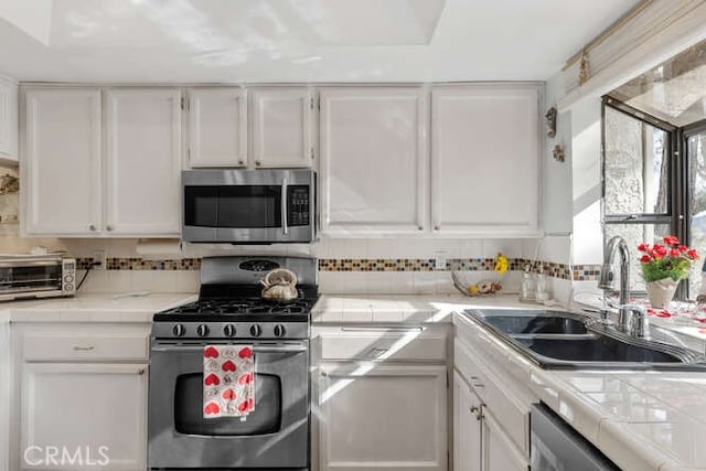 kitchen with sink, tile counters, stainless steel appliances, decorative backsplash, and white cabinets