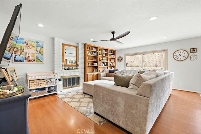 living room featuring a brick fireplace, a textured ceiling, light hardwood / wood-style flooring, and ceiling fan