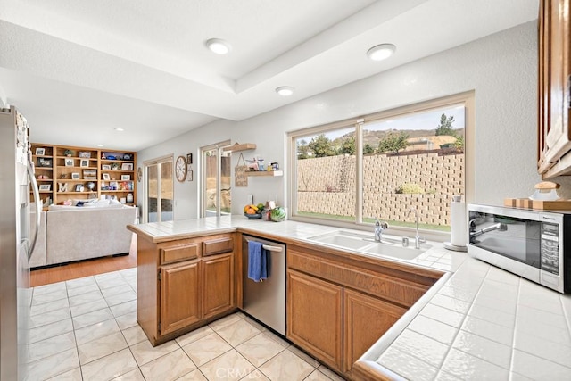 kitchen featuring appliances with stainless steel finishes, sink, tile counters, light tile patterned floors, and kitchen peninsula