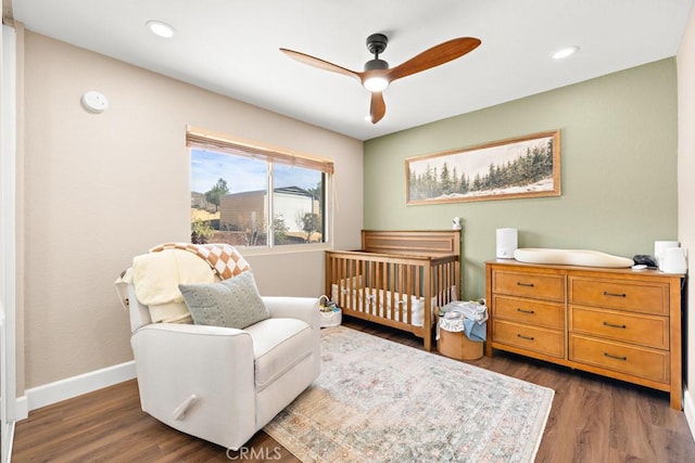 bedroom with a crib, ceiling fan, and dark hardwood / wood-style flooring