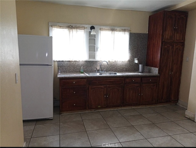 kitchen featuring sink, dark brown cabinets, light tile patterned floors, white fridge, and backsplash