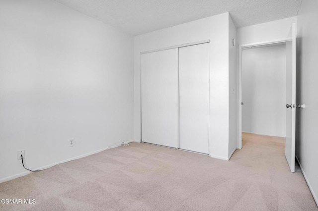 unfurnished bedroom featuring light colored carpet, a textured ceiling, and a closet