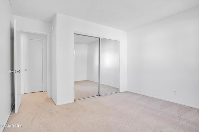 unfurnished bedroom featuring light carpet, a textured ceiling, and a closet