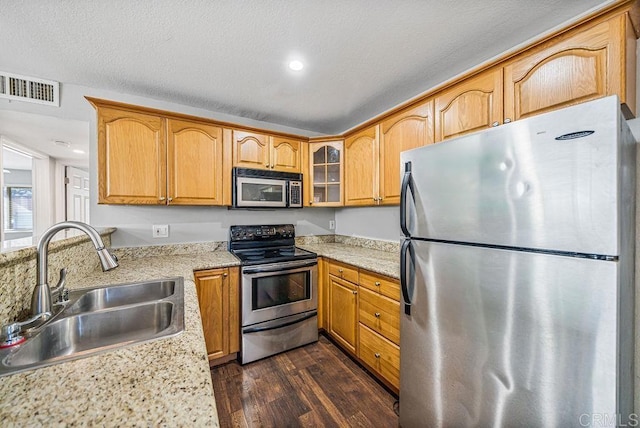 kitchen with dark wood-type flooring, sink, a textured ceiling, stainless steel appliances, and light stone countertops