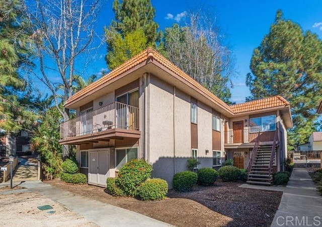 view of side of home featuring stairway, a tile roof, and stucco siding