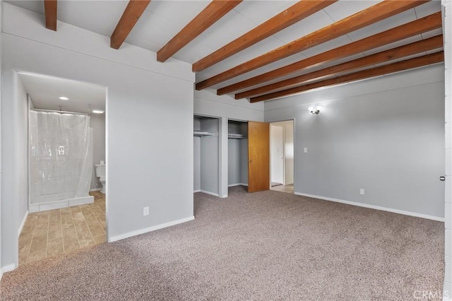 unfurnished bedroom with beamed ceiling, a closet, connected bathroom, and carpet