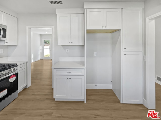 kitchen with stainless steel appliances, white cabinetry, and light hardwood / wood-style flooring