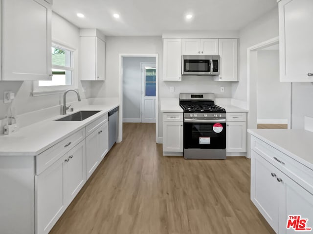 kitchen featuring stainless steel appliances, sink, white cabinets, and light wood-type flooring