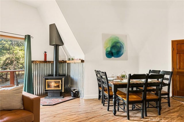 dining space with high vaulted ceiling, light hardwood / wood-style flooring, and a wood stove