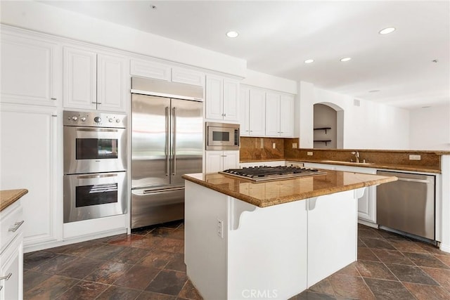 kitchen featuring stone countertops, white cabinets, built in appliances, and a center island