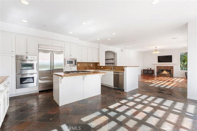 kitchen with built in appliances, tasteful backsplash, white cabinets, a breakfast bar, and a kitchen island