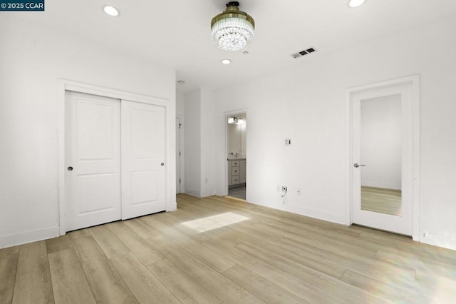 unfurnished bedroom featuring an inviting chandelier, a closet, ensuite bathroom, and light hardwood / wood-style flooring